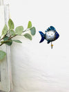 Lifestyle image of blue fin fish hook hanging on a wall near greenery.