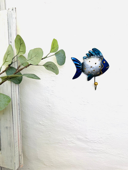 Lifestyle image of blue fin fish hook hanging on a wall near greenery.