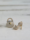 Gold high-heeled shoe and studded handbag charm on a light wooden surface