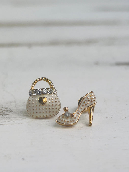 Gold high-heeled shoe and studded handbag charm on a light wooden surface