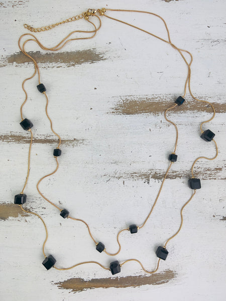 A double strung necklace with black crystal cubes on a wooden surface.