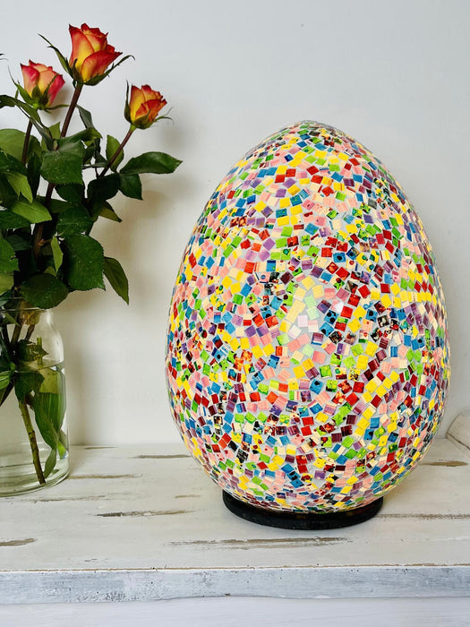 front view of mosaic egg lamp light on with vase of roses next to lamp