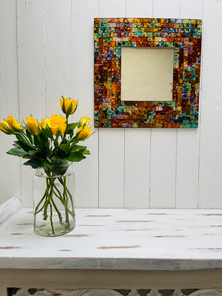 front view of mosaic square mirror hung on the wall with a vase of yellow roses on a table below