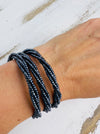 A gunmetal-coloured seed bead bracelet with a plaited effect and shell detail at each end, displayed on a model.