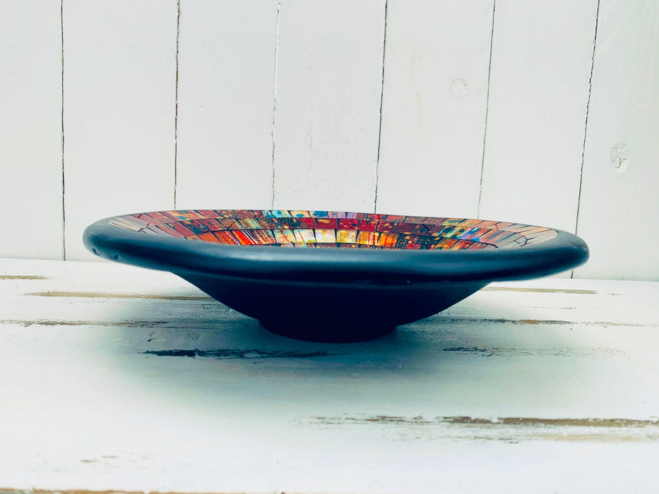 Side view of handmade mosaic Calypso bowl showing terracotta base and glossy warm-toned glass mosaic on white wooden surface.
