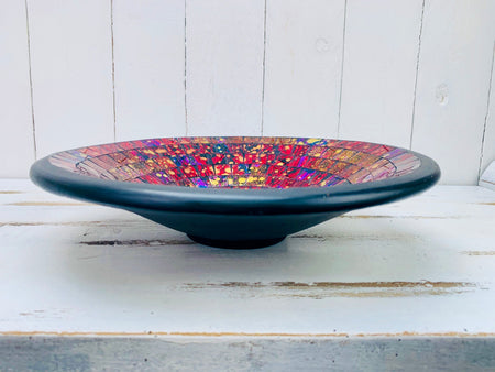 Side view of handmade mosaic glass bowl in Violet Burst colours showing curved terracotta base and glossy red and purple surface.