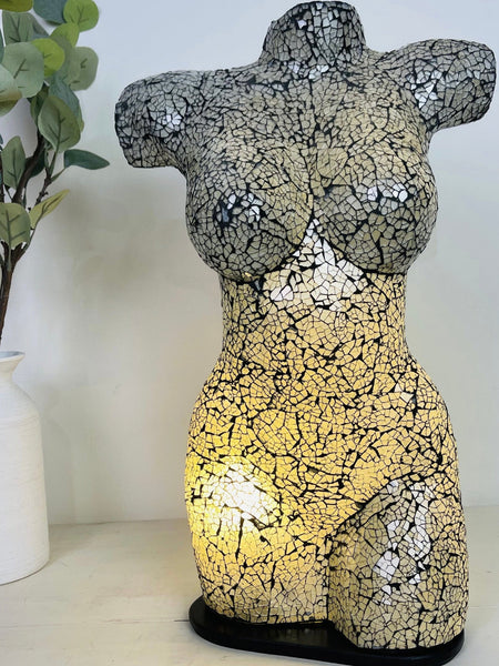 Handmade mosaic bust lamp illuminated in silver tones beside green plant in white vase on white table, showing crackle glass pattern.