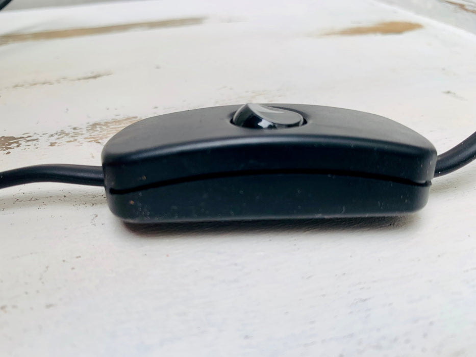 Close-up of black inline switch and cable with UK plug on white wooden background for handmade mosaic lamp.