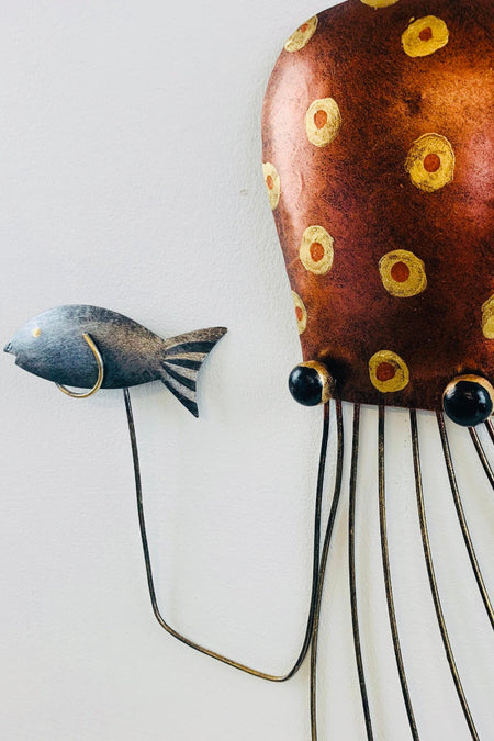 Angled view of copper metal octopus showing hand-painted detailing and small fish accent