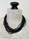 A black beaded necklace draped over a book-page-covered mannequin neck with a black spherical top, photographed against a plain light background.