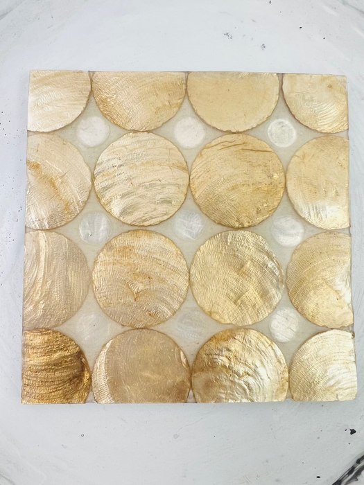 Handmade shell coaster with cream and gold tones, consisting of various circular shells arranged in a pattern on a flat surface.