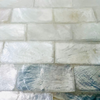 Close-up of white and pearlescent shell tiles arranged in a brick pattern with glossy resin coating.