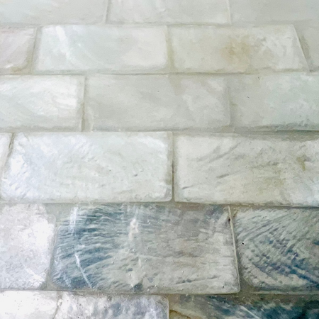 Close-up of white and pearlescent shell tiles arranged in a brick pattern with glossy resin coating.