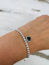 Silver beaded bracelet with a black heart charm on a wrist against a white background