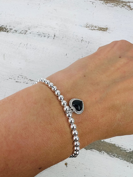 Silver beaded bracelet with a black heart charm on a wrist against a white background