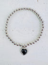 Silver bracelet with a black filigree heart detail, presented against a white background.