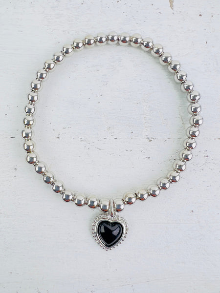 Silver bracelet with a black filigree heart detail, presented against a white background.