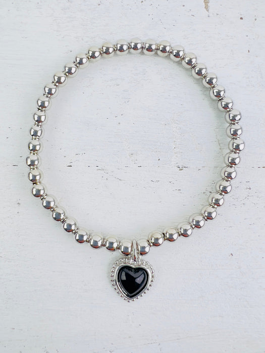 Silver bracelet with a black filigree heart detail, presented against a white background.