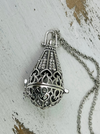 Silver ornate pendant on a chain against a textured white background