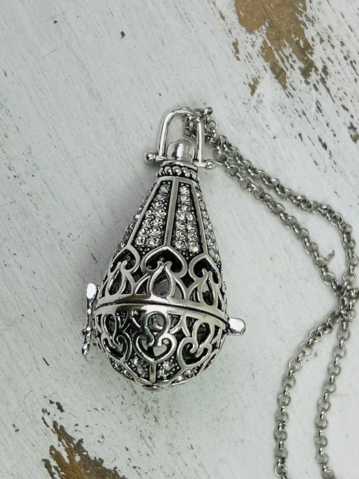 Silver ornate pendant on a chain against a textured white background