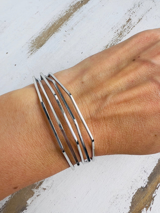 A silver bracelet with a geometric wave design, displayed on a person's wrist.