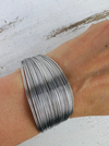 A silver-plated cuff bracelet worn on a wrist, displaying its multilayered design.