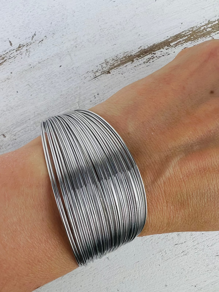 A silver-plated cuff bracelet worn on a wrist, displaying its multilayered design.