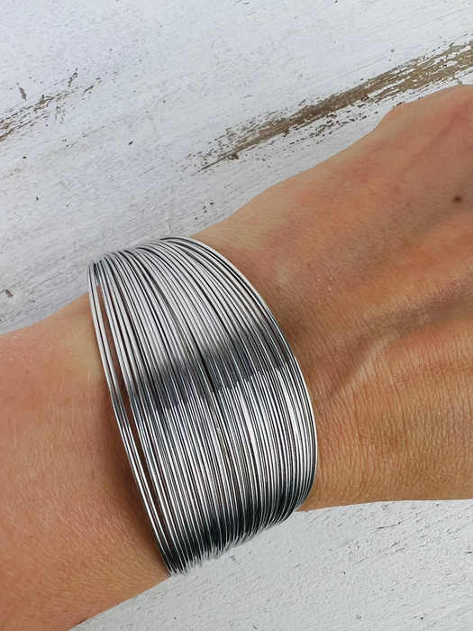 A silver-plated cuff bracelet worn on a wrist, displaying its multilayered design.