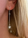 A close-up image of a woman's ear wearing a silver drop earring with a star-shaped pendant.