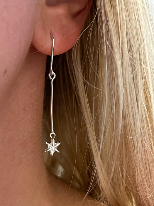 A close-up image of a woman's ear wearing a silver drop earring with a star-shaped pendant.
