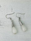 Pair of silver earrings with teardrop-shaped white stones on a textured gray background