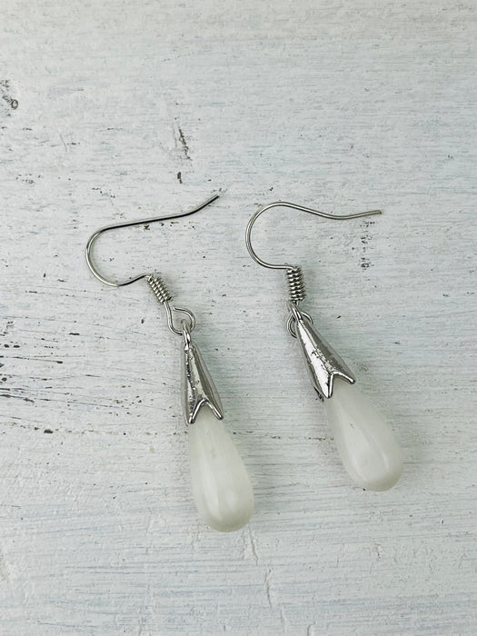 Pair of silver earrings with teardrop-shaped white stones on a textured gray background