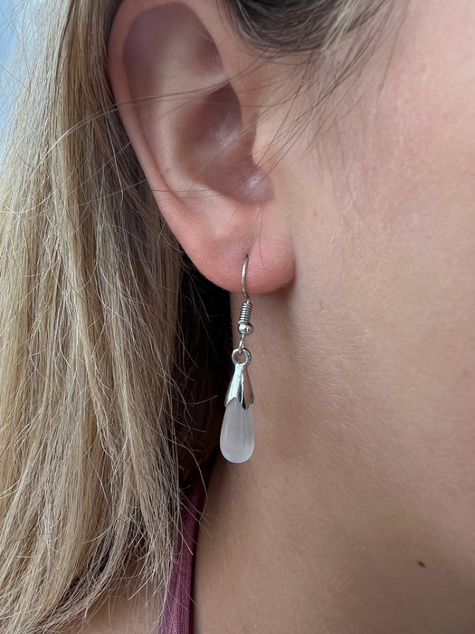 A close-up image of a person wearing silver teardrop earrings with a cats eye detail.