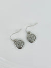 A pair of silver-colored earrings with a simple cross diamond pattern and tiny crystal detail, displayed on a white background.