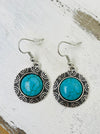 A pair of round style synthetic turquoise earrings with intricate designs around the stone, attached to fish hook ear wires.