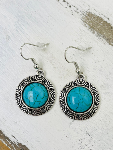 A pair of round style synthetic turquoise earrings with intricate designs around the stone, attached to fish hook ear wires.