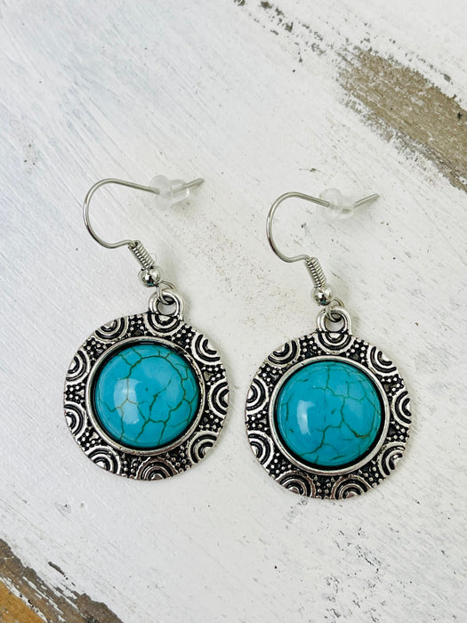 A pair of round style synthetic turquoise earrings with intricate designs around the stone, attached to fish hook ear wires.