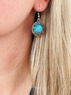 Close-up of a turquoise earring with silver detailing worn by a person with blonde hair.