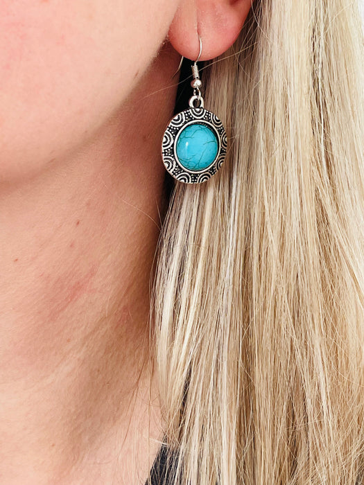 Close-up of a turquoise earring with silver detailing worn by a person with blonde hair.