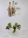 Metal wine bottle and glass wall art displayed above a table with flowers