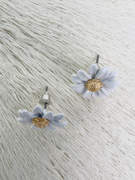 A pair of daisy flower stud earrings with white petals and a gold-colored center, displayed against a textured white background.